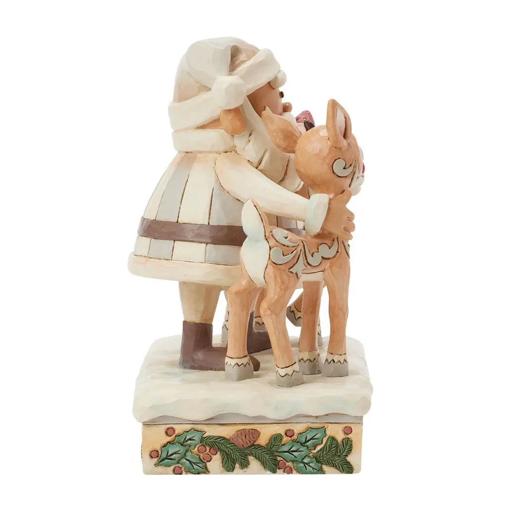 Side view of Jim Shore cream Santa figurine hugging reindeer with carved scroll patterns, standing on snow-covered base decorated with holly and pinecones.