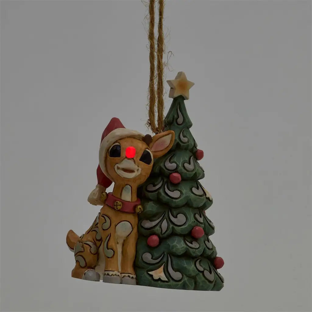 Jim Shore woodland Rudolph ornament with light-up red nose, wearing Santa hat beside decorated Christmas tree.
