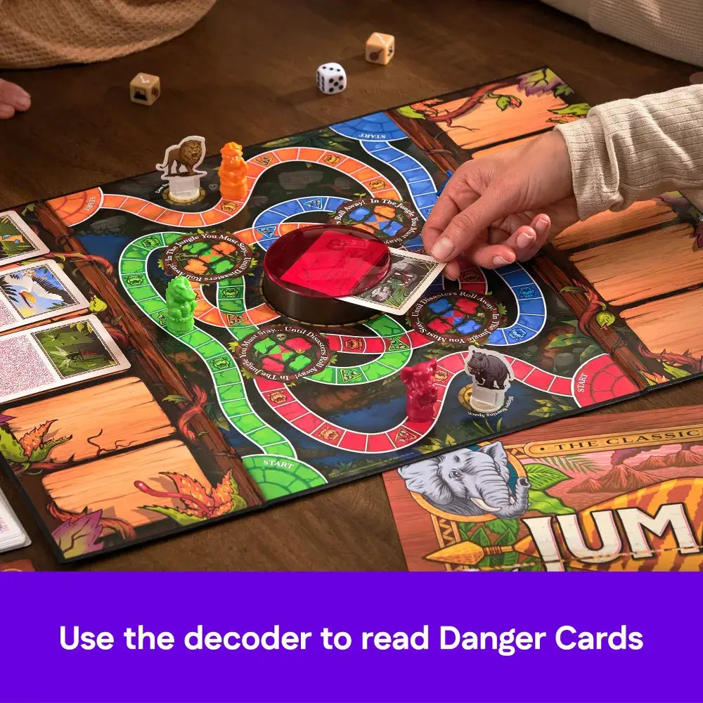 Jumanji adventure board game with colorful jungle path, dice, animal figurines, and red decoder lens revealing text on danger cards as players move pieces.