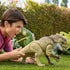 A child plays outside with the Jurassic World Distortus Rex figure, gripping its tail as the large beige-and-brown dinosaur stands on grass with detailed sculpting and lifelike textured skin.