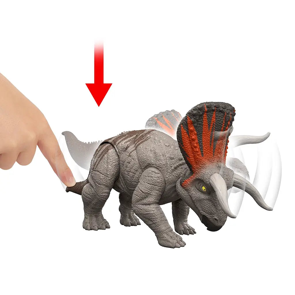 Jurassic World Zuniceratops Strike Attack feature shown in gray plastic with orange frill as a hand presses the tail, demonstrating head and frill motion for action play, illustrated on a clean white background.