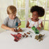 Two smiling children sit at a white table, using a teal toy drill to assemble colorful screw-together dinosaur toys with parts and tools spread out around them.