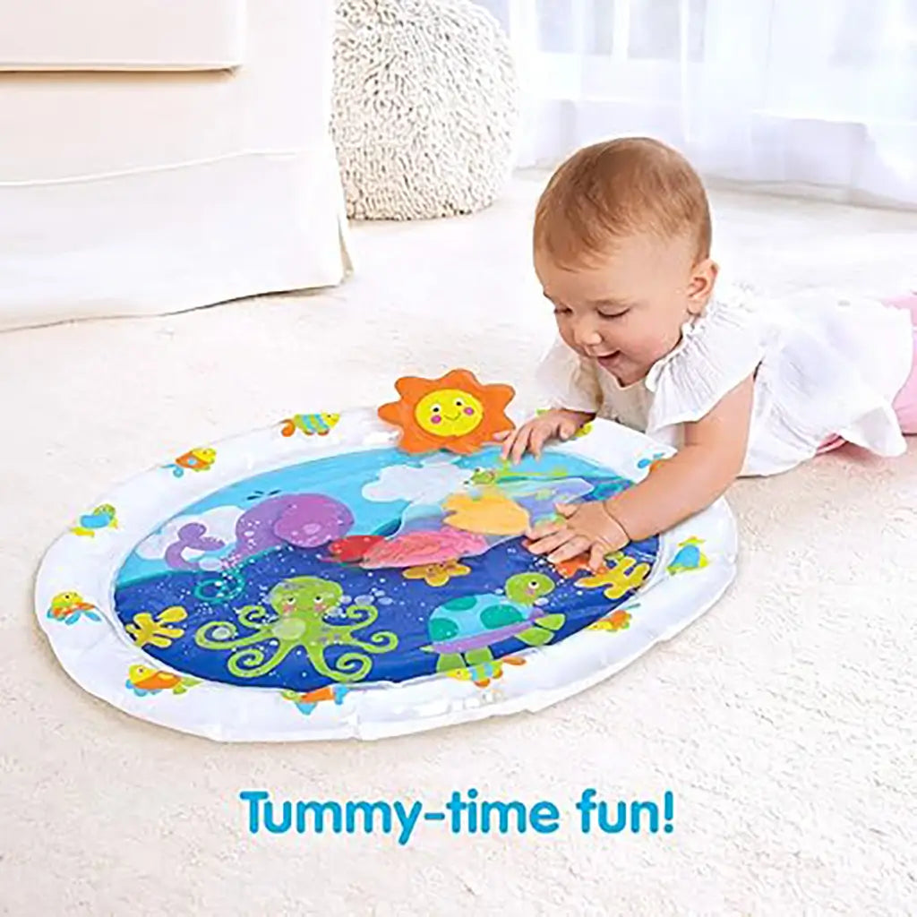 Baby in white outfit enjoys tummy time on Kidoozie Pat 'n Laugh Water Mat, pressing colorful floating sea animals inside the soft water-filled play mat for sensory fun.
