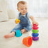 Smiling baby boy in denim overalls sits on beige carpet, stacking colorful Kidoozie cups into a tower while holding a yellow piece, engaging in motor skill and coordination play.