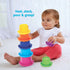 Young toddler girl in white top and red pants sits on carpet stacking Kidoozie cups into a tall tower, smiling as she practices coordination, grasping, and early learning play.