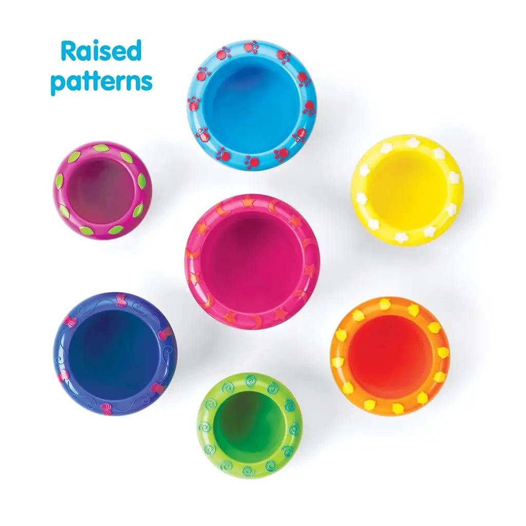 Overhead view of seven colorful Kidoozie stacking cups in blue, yellow, pink, orange, green, red, and purple, each featuring unique raised rim patterns for added texture and play variety.