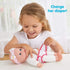 Smiling girl in a white top changes the diaper of a Kidoozie Sweetie Doll dressed in pink pajamas with floral embroidery and matching headband on a white table.