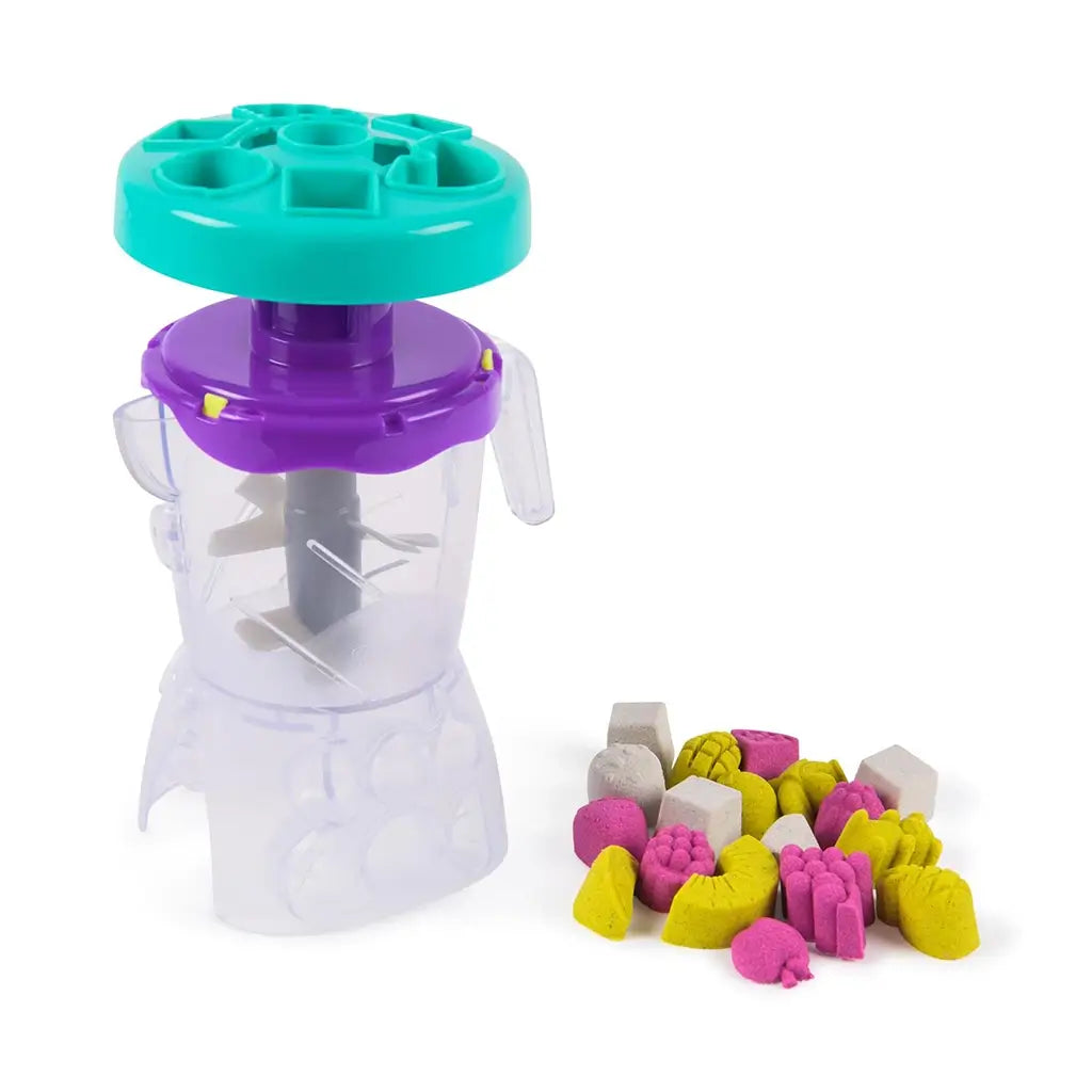 Clear plastic Kinetic Sand Smoothie Mixer blender with purple collar, teal lid, internal gray blades, and sturdy base, designed for hands-on mixing and imaginative sensory play on white background.