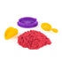 Kinetic sand playset in red crumbly texture with purple mold ring and yellow plastic scoop tools, arranged as a pretend food kit for shaping and serving play on a white background.