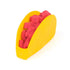 Kinetic sand taco toy in red crumbly texture packed inside a bright yellow plastic shell with curved form, designed for pretend food play and shaping activities on a clean white background.