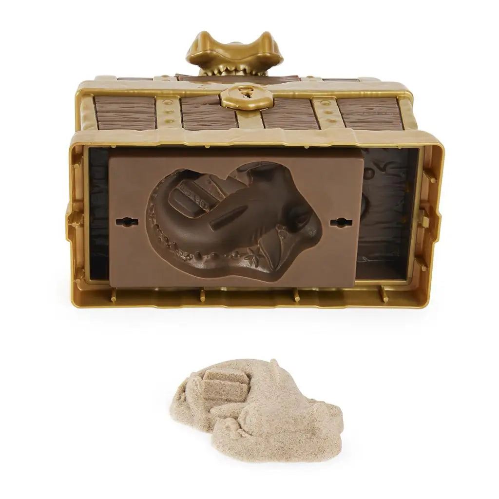 Brown and gold Kinetic Sand treasure chest underside showing hidden shark-shaped mold compartment, molded plastic details, and removable sand pieces for surprise discovery play on white.