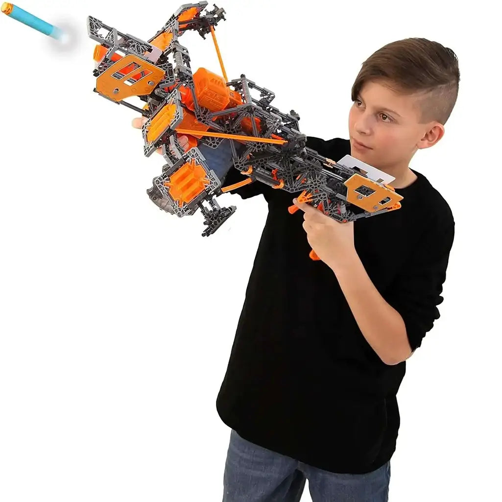 Child holding and aiming a large blaster built from the K'NEX Cyber-X C10 Legacy set, launching a foam dart for action-packed pretend play.