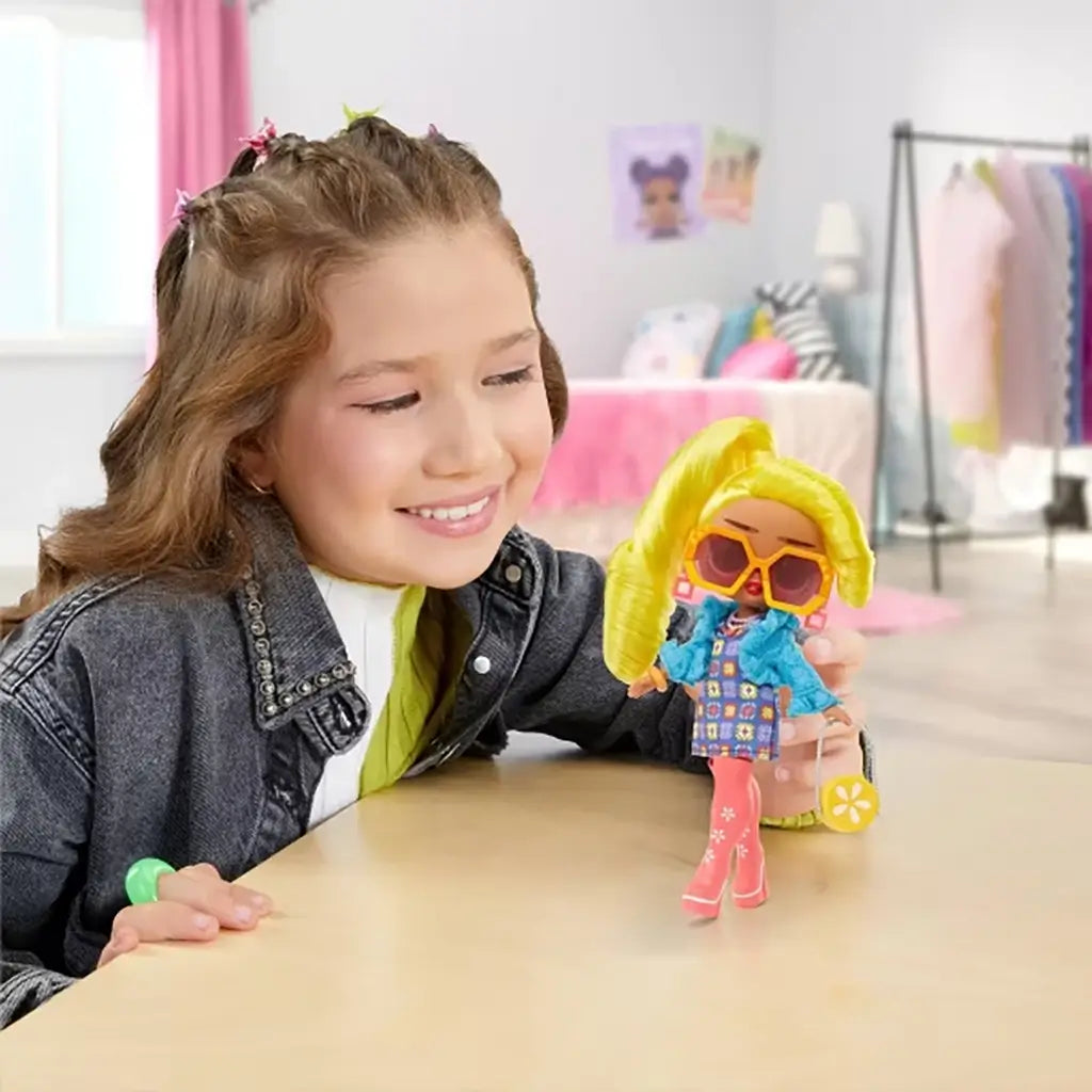 Smiling child holding the LOL Surprise Tweens Hana Groove doll with bright yellow hair, pink boots, and blue jacket in a cozy bedroom decorated with soft pink tones and playful wall art.