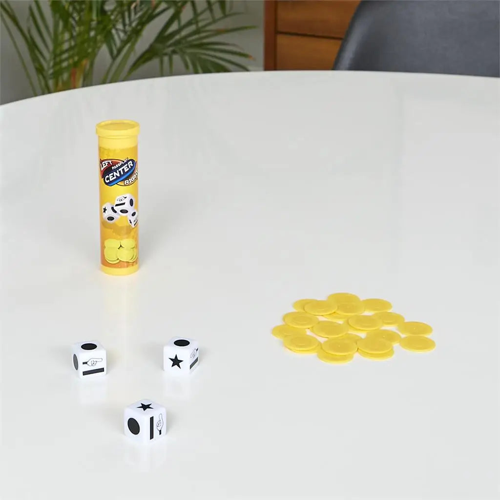 Left Center Right travel dice game in yellow tube with white dice and stacked yellow chips, displayed on a white tabletop in a bright indoor setting.