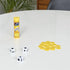 Left Center Right travel dice game in yellow tube with white dice and stacked yellow chips, displayed on a white tabletop in a bright indoor setting.