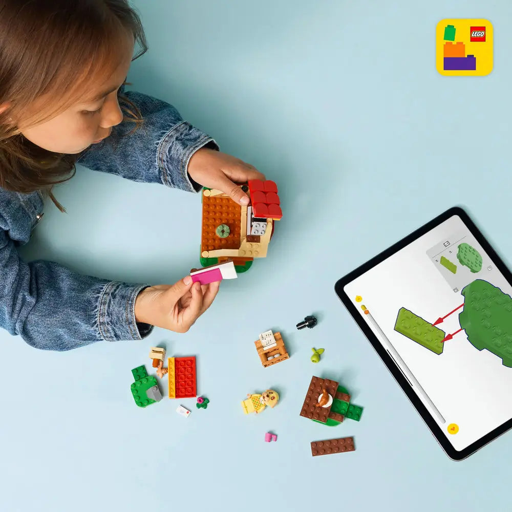 LEGO Animal Crossing Goldie's Cozy House playset shows a child assembling the tan cottage with digital building instructions on a tablet across a light blue tabletop with detailed LEGO elements and realistic display presentation.