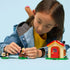 LEGO Animal Crossing Goldie's Cozy House playset features a child playing with the tan cottage, Goldie character and outdoor accessories on a light blue background with detailed LEGO elements and realistic display presentation.