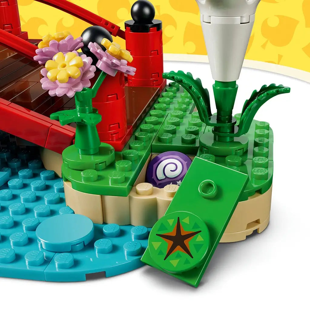 LEGO Animal Crossing hidden fossil feature in green, tan, blue, red, and purple plastic shows a hinged grass panel revealing a spiral fossil beside flowers and the stream.
