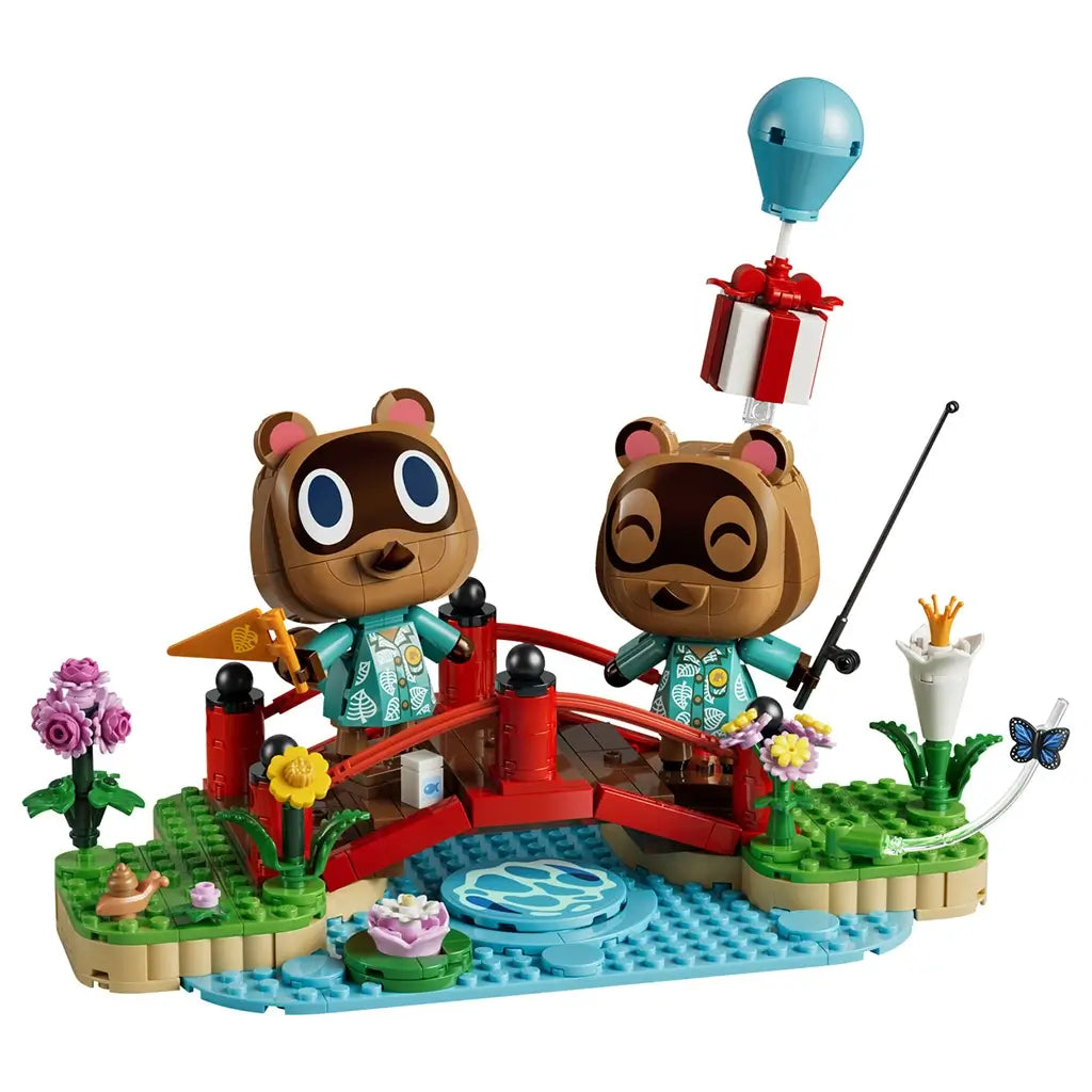 LEGO Animal Crossing Timmy & Tommy playset in red, green, blue, brown, and pink plastic features two raccoon figures on a bridge with flowers, stream, fishing rod, and balloon gift.