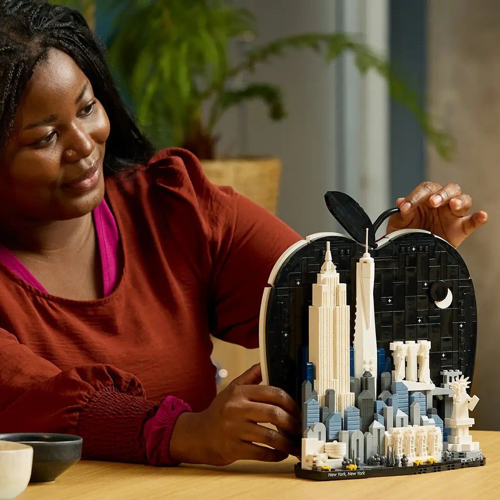 LEGO Architecture New York City display uses black, white, gray and blue plastic bricks as an adult holds the finished Big Apple skyline model on a wooden table.