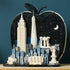 LEGO Architecture New York City model uses black, white, gray and blue plastic bricks to form an apple-shaped skyline with famous landmarks against a teal wall.