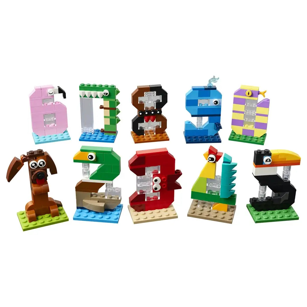 LEGO birthday numbers toy in pink, green, brown, blue, purple, red and black plastic brick forms, shaped as animal-themed digits 0–9 for party decor on a plain studio background.
