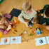 LEGO Bluey Brick-Built Family set in blue, orange, brown, and yellow plastic is assembled by two children at a wooden table, with loose accessories and instructions nearby.