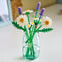 LEGO Botanicals Daisies display showing completed white daisy and lavender bouquet with green stems, elegant plastic brick floral arrangement for home decor, placed in a clear glass jar.