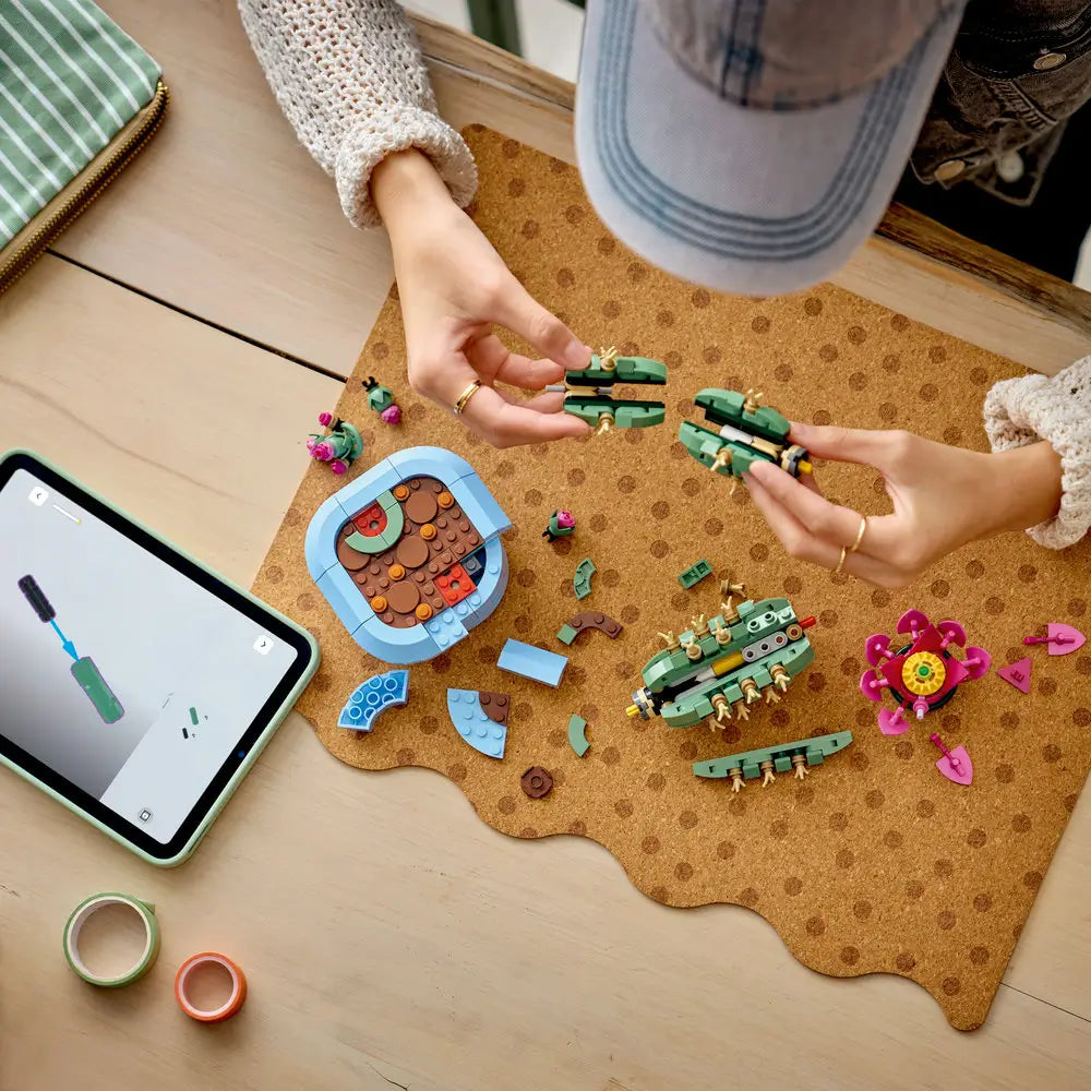 LEGO Botanicals Flowering Cactus lifestyle build image showing partially assembled green plastic cactus segments with beige spines, curved modular forms for mindful building, laid out on a table beside digital instructions.