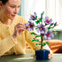 Builder in a yellow sweater adding small LEGO leaf pieces to the Botanicals Hibiscus plant, with parts and instructions neatly arranged on the table.