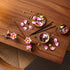 LEGO magnolia branches build features pink and white plastic petals, brown stems, and small green buds, arranged as a floral assembly project on a wooden table with tools and parts in a home crafting setting.