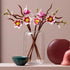 LEGO magnolia branch display features pink and white plastic flowers with yellow centers on brown stems in a clear glass vase, styled as modern floral home decor on a tabletop with minimal background.