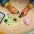 LEGO Botanicals Rocking Plants set in pink, green and light green bricks is assembled by a child, with flower stems, planter pieces and instructions spread on a wood table.