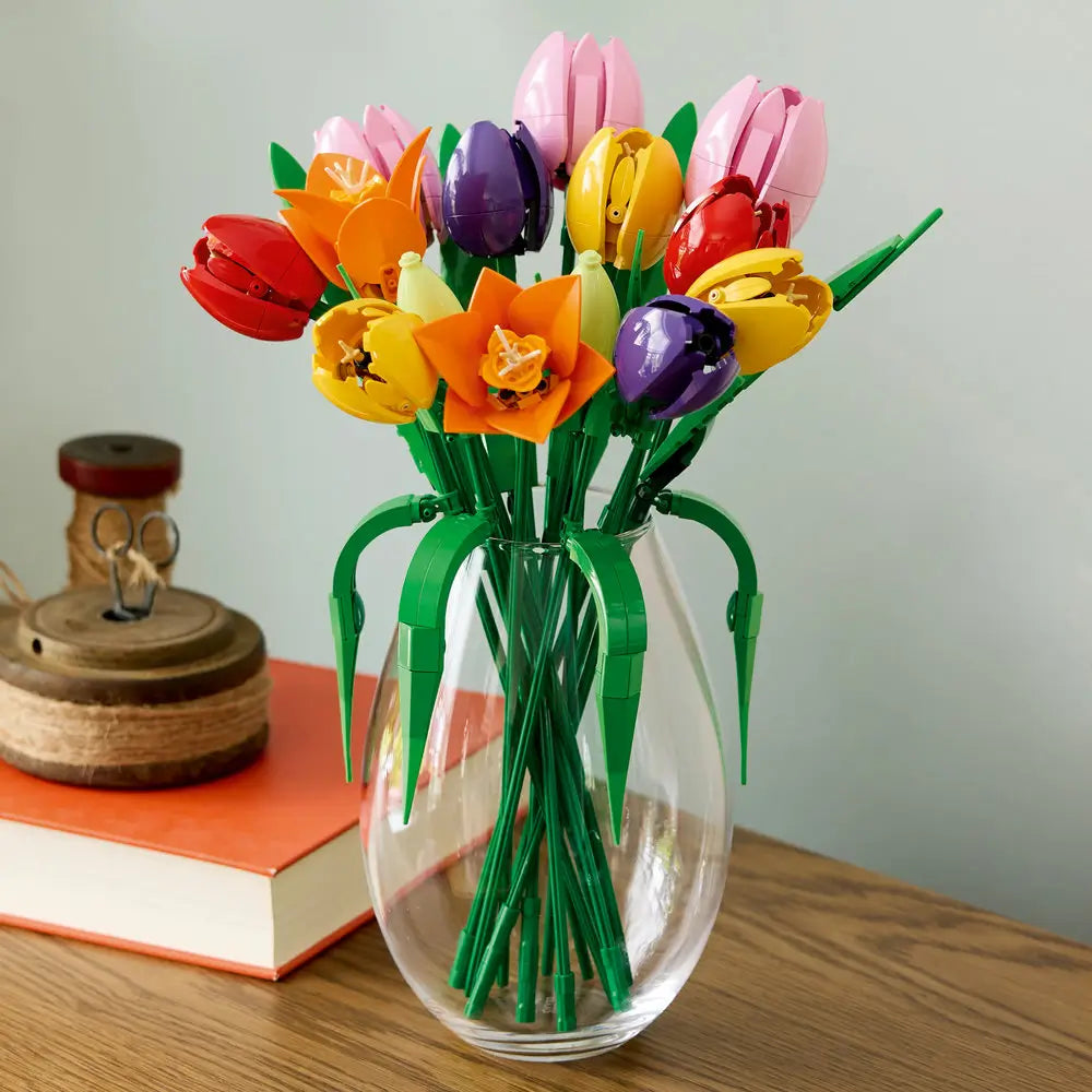 LEGO tulip bouquet displayed in a clear glass vase features multicolored plastic flowers with smooth petals and tall green stems, styled as a decorative centerpiece on a wooden surface indoors.