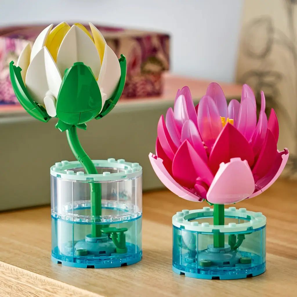 LEGO Botanicals Water Lilies in white, yellow, pink, purple, green, and clear plastic stand in two cylindrical display bases on a wooden shelf in a home setting.