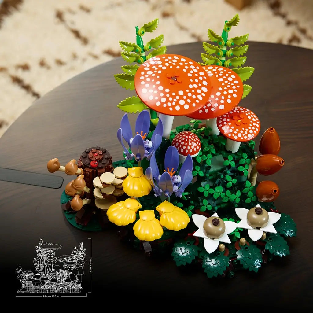 LEGO Botanicals Woodland Mushrooms display features orange spotted caps, yellow and brown fungi, purple flowers, and green plastic foliage arranged on a dark tabletop.