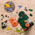 LEGO Botanicals Woodland Mushrooms pieces in orange, yellow, purple, brown, white, and green plastic are spread across a stone surface around a partly built forest base.