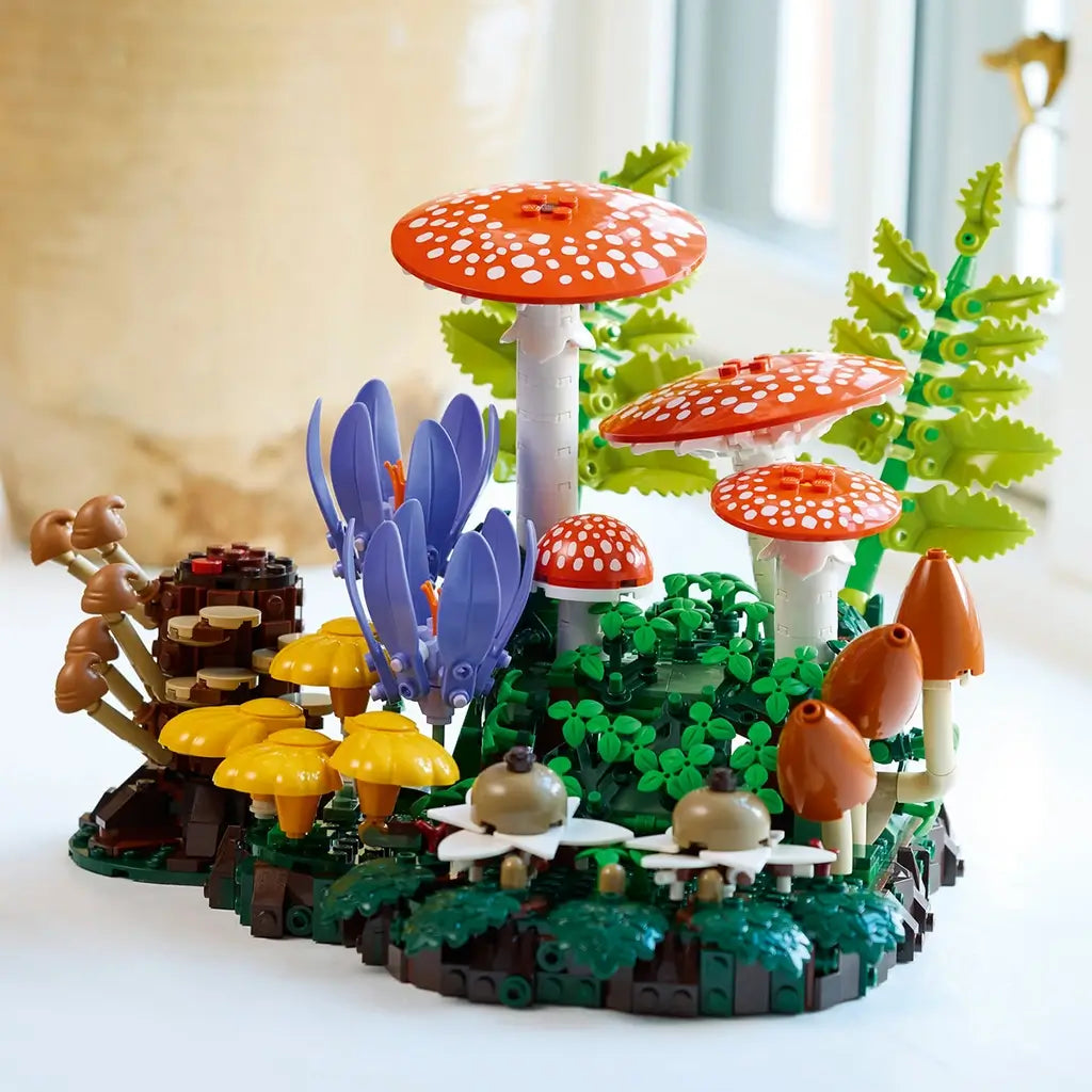 LEGO Botanicals Woodland Mushrooms display combines orange spotted caps, yellow and brown fungi, purple flowers, and green plastic ferns in a detailed forest scene.