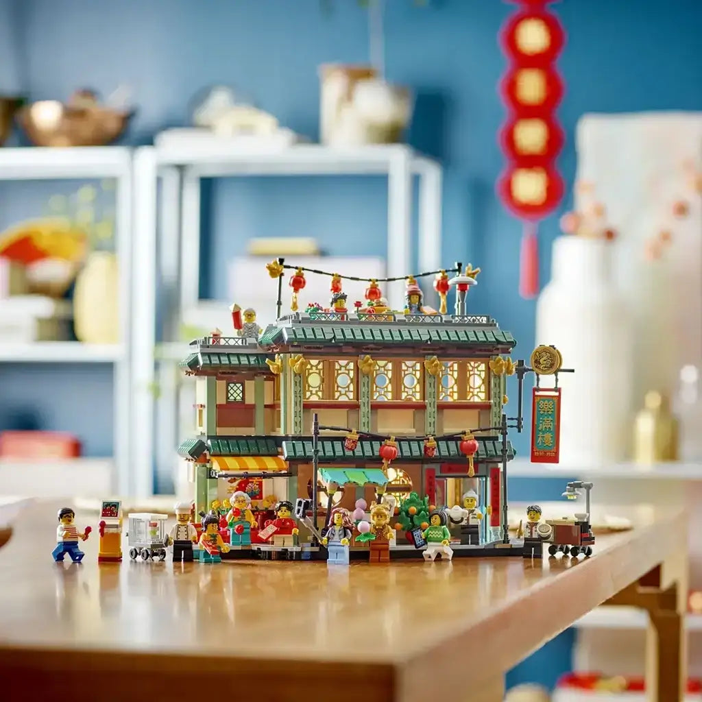 LEGO Spring Festival 80113 restaurant in green, red, gold and tan plastic is displayed with lanterns, minifigures and food carts on a wooden table in a bright room.