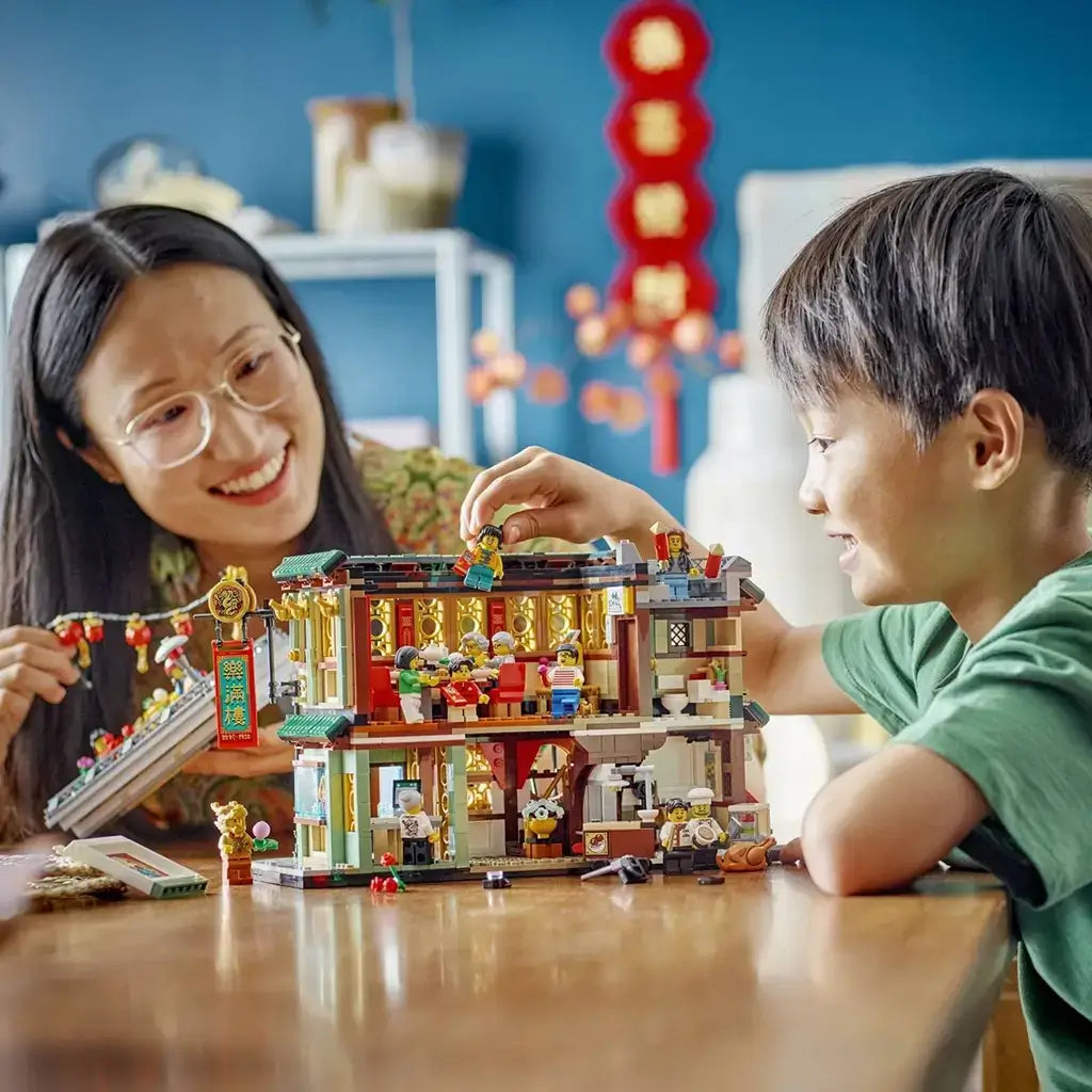 LEGO Spring Festival set in green, red, gold and tan plastic shows a child and adult playing with the open Family Reunion Celebration restaurant on a wooden table.