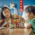 LEGO Spring Festival set in green, red, gold and tan plastic shows a child and adult playing with the open Family Reunion Celebration restaurant on a wooden table.