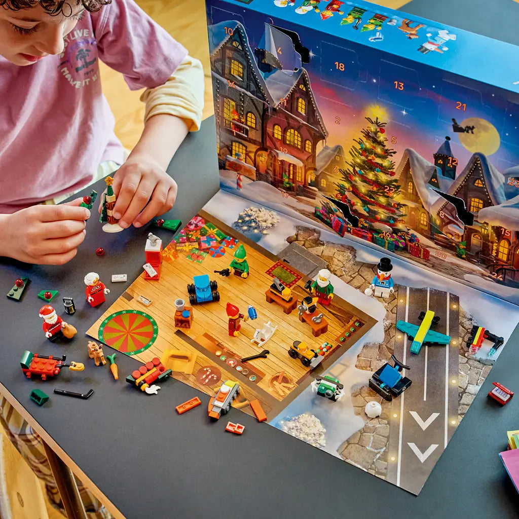 LEGO City Advent Calendar 2026 play set features colorful plastic holiday figures and toy builds spread across a workshop play mat as a child assembles a Christmas tree.