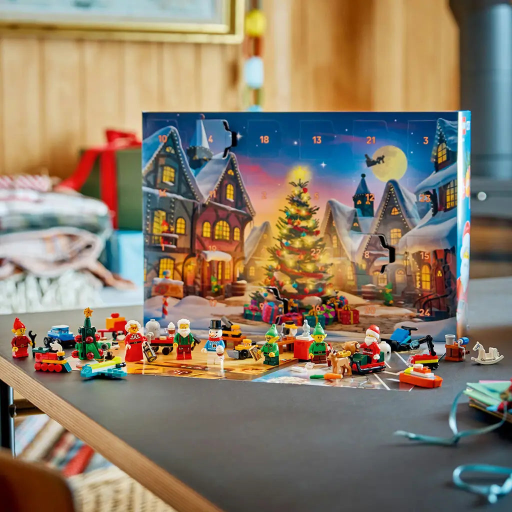 LEGO City Advent Calendar 2026 display features colorful plastic Santa, elves, snowman, Christmas tree and toy builds arranged before the numbered snowy village calendar.