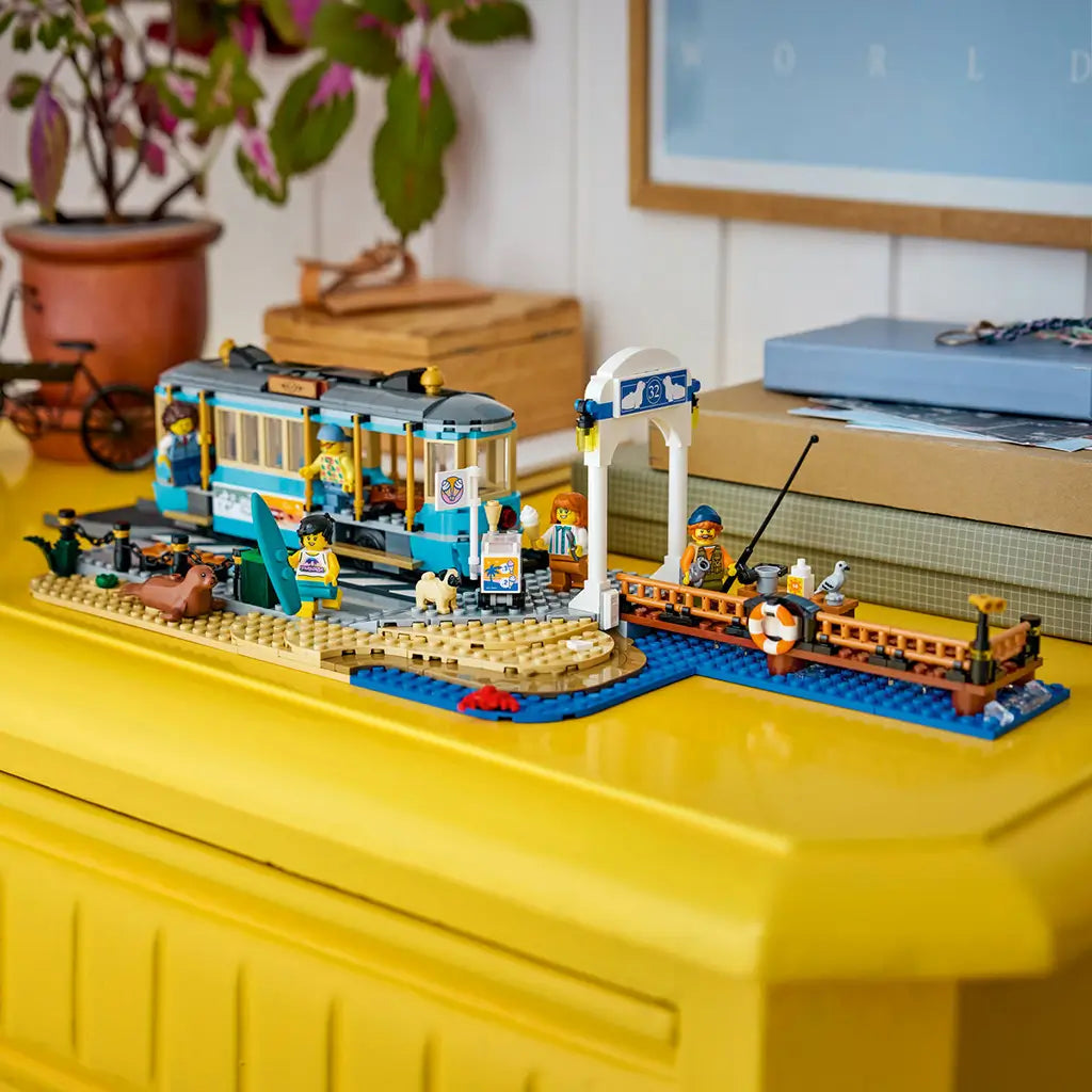 LEGO City Classic Beach Streetcar in turquoise, tan, gray, blue, and brown plastic bricks displays a tram, beach stop, fishing pier, minifigures, dog, seal, and surfboard.