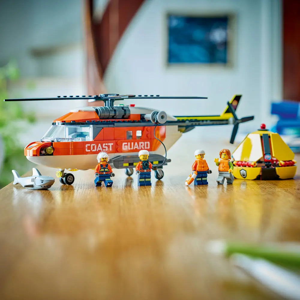 LEGO City Coast Guard helicopter displayed with minifigures, shark, and yellow lifeboat pod, featuring orange and white body details, arranged neatly on a tabletop for completed model showcase.