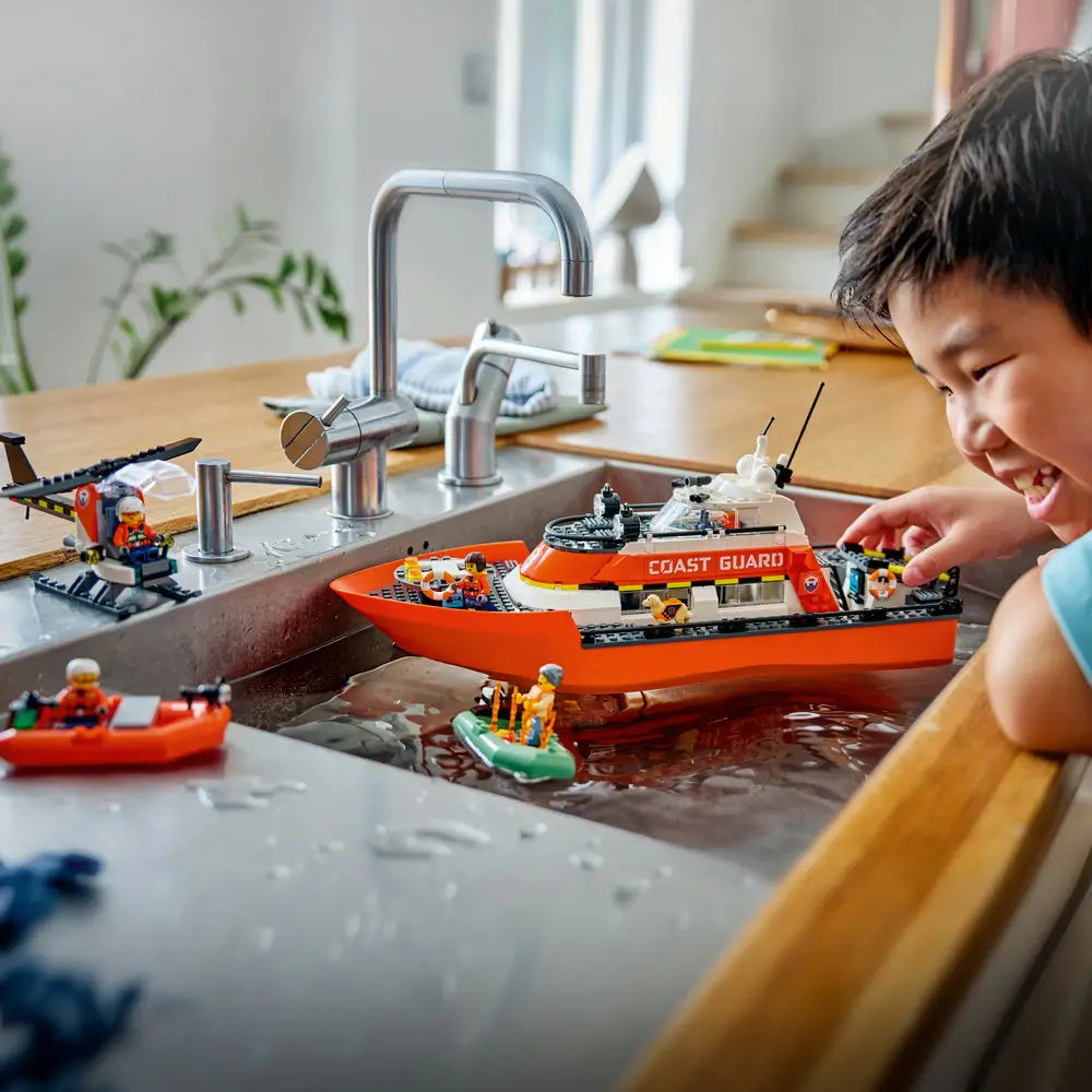 LEGO City lifestyle image of a child playing with the Coast Guard rescue boat in a kitchen sink, demonstrating floating play, rescue scenarios, and hands-on imaginative water-based fun at home.