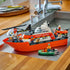 LEGO City Coast Guard rescue boat displayed with helicopter and dinghy, featuring orange hull, white cabin, minifigures, and fire rescue elements, arranged on a countertop for completed model showcase.