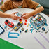 LEGO City Drive-Through Car Wash in teal, white, red, and gray plastic bricks is assembled by a child at a table with two cars, minifigures, brushes, and loose pieces.