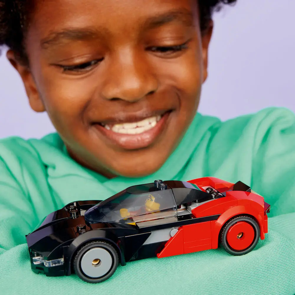 LEGO City EV Supercar lifestyle scene showing a smiling child holding the completed black and red electric sports car toy, smooth curved body, wide wheels, and enclosed cockpit against a soft studio background.