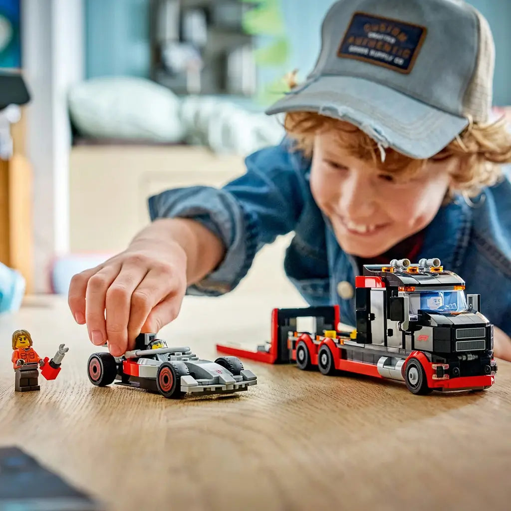 LEGO City race car playset in red, black, and gray plastic, flatbed truck and Formula 1 car models, child assembling toy vehicles on a wooden table in a bright indoor setting.